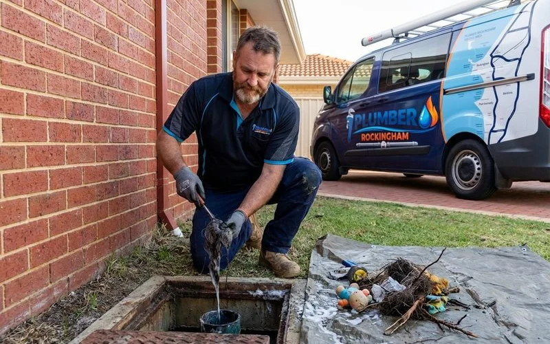 Plumber removing foreign objects and debris from a blocked drain pipe at a Rockingham residential property